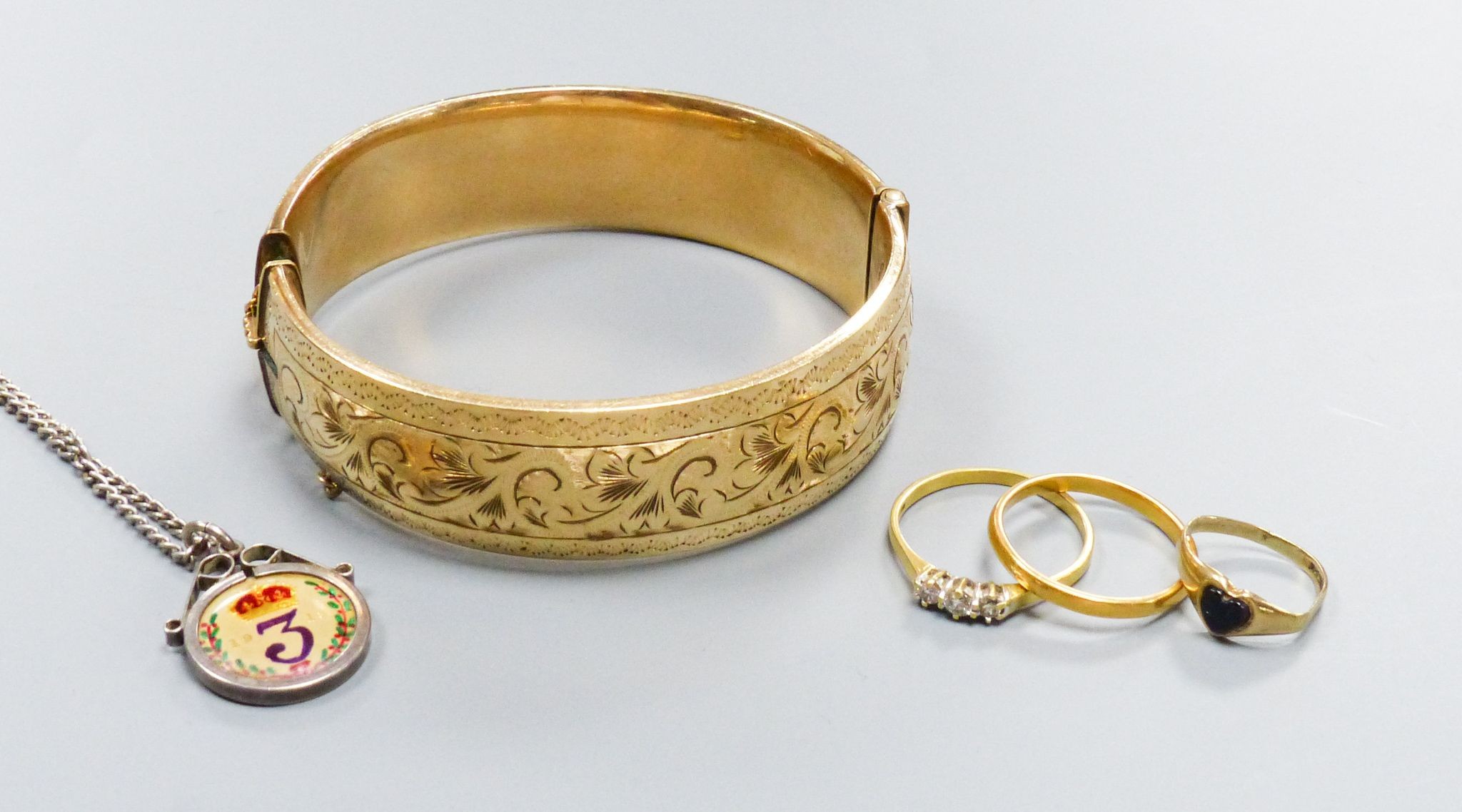 A filled 9ct gold (metal core) bangle together with a three-stone 18ct yellow gold diamond ring (gross 2.6g) a 22ct yellow gold wedding band (3.1g) and a further small gold ring and an enamelled coin pendant on chain (5)